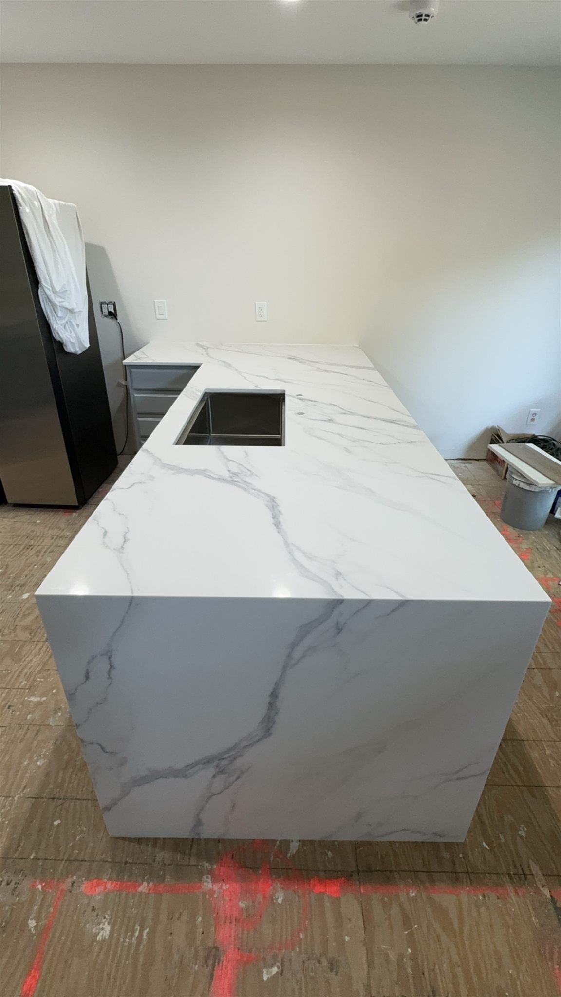 Calacatta-look island with a mitered waterfall end and an undermount sink, bold grey veins running over the corner and down the side