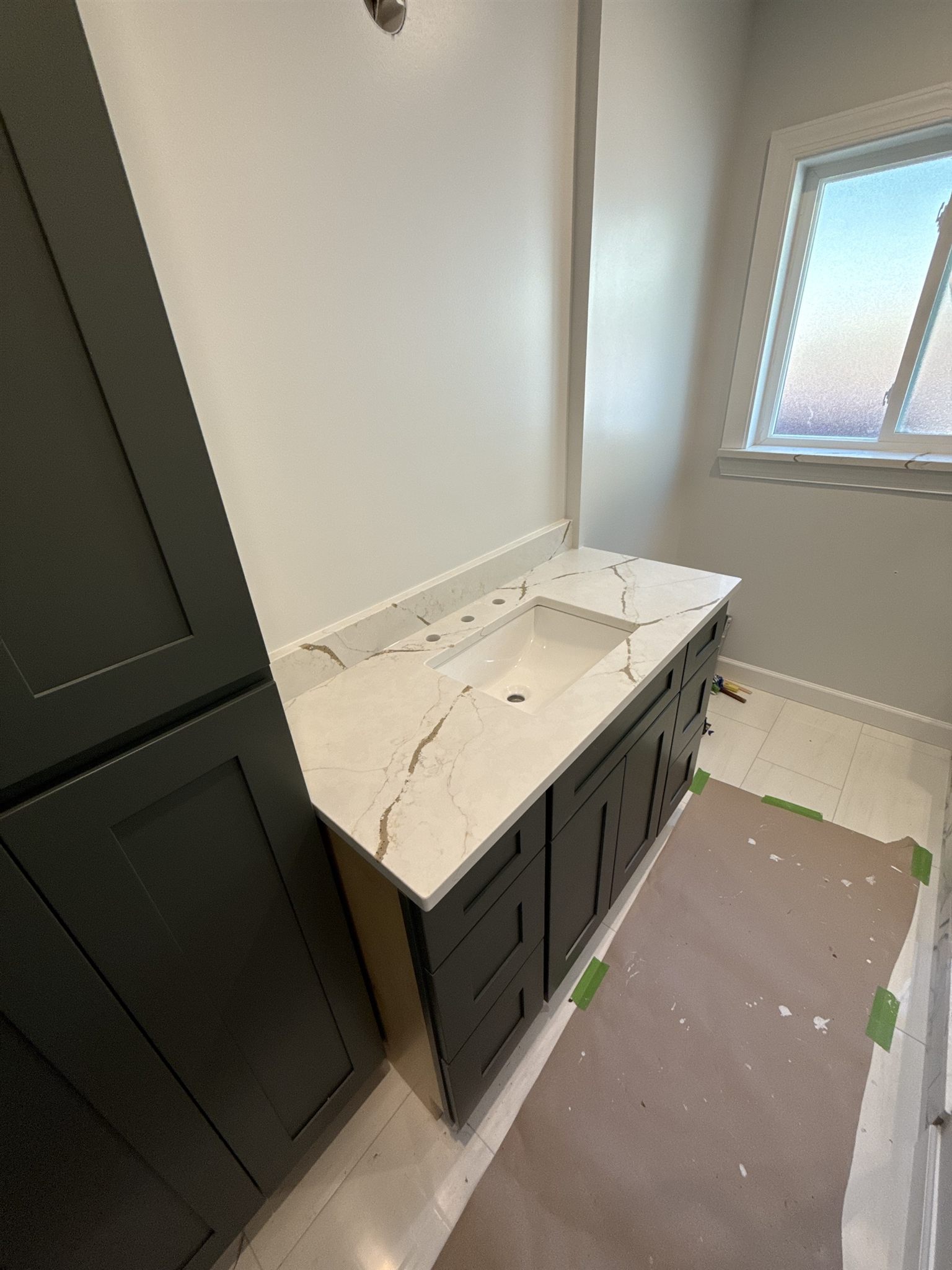 White quartz vanity top with gold veining and an undermount sink on a dark green shaker vanity