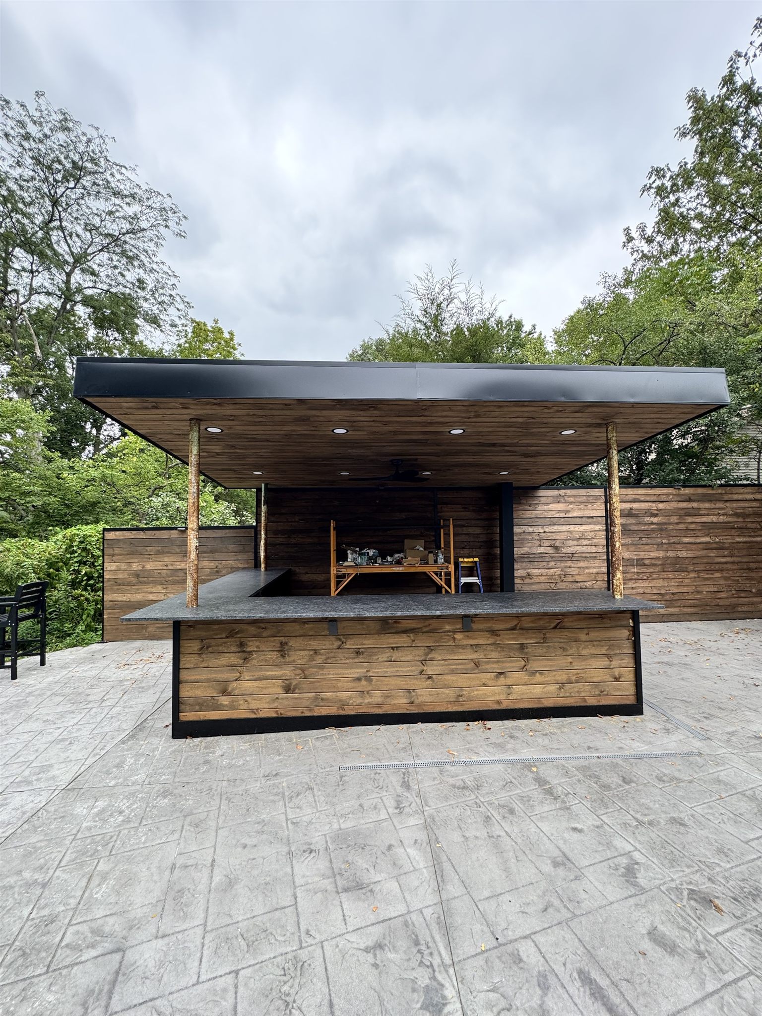 Outdoor L-shaped bar with a dark granite top under a covered cedar pavilion