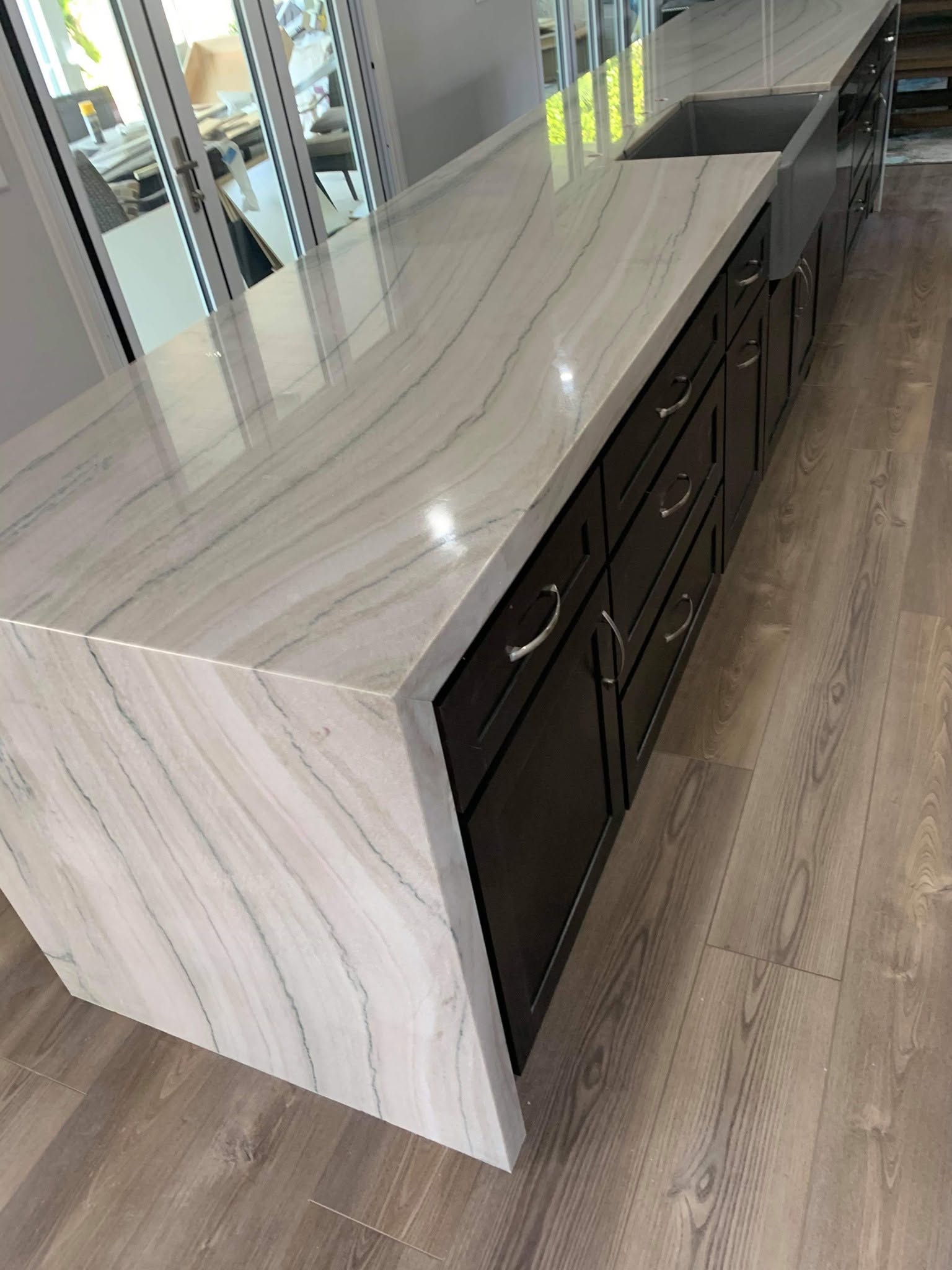 Quartzite waterfall island with long grey veins over dark shaker cabinets